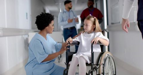Nurse Supporting Wheelchair-Bound Child in Hospital Corridor