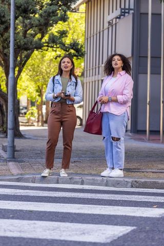 African american friends standing at curb waiting at urban crosswalk holding red tote
