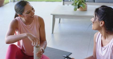 Diverse women smiling and hydrating after workout on sunlit patio