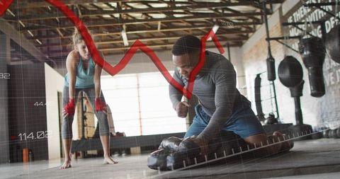 Kneeling athlete delivering powerful punch to heavy bag in industrial gym with data overlay