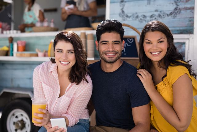 Group of friends smiling and enjoying time together at a food truck. Perfect for themes related to friendship, social gatherings, outdoor activities, and urban lifestyle. Ideal for use in advertisements, social media posts, and promotional materials for food trucks, events, and lifestyle brands.