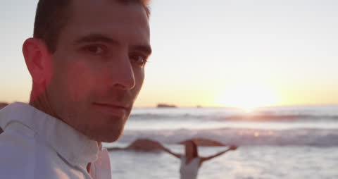 Man Contemplating on Beach at Sunset with Woman in Background