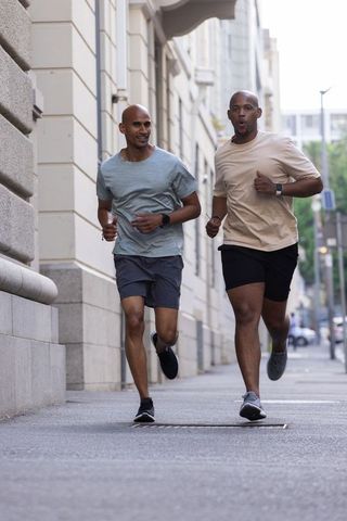 African american friends jogging together on city sidewalk wearing fitness watches