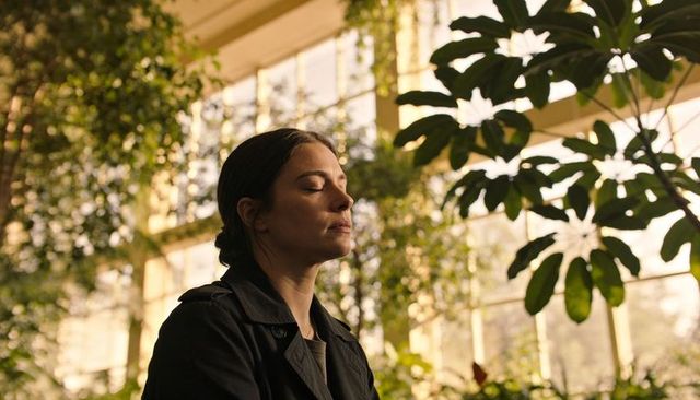 Woman in greenhouse breathing deeply during golden hour surrounded by lush hanging vines