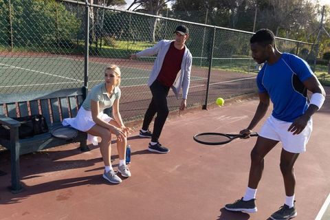 Diverse friends practicing tennis drills on sunny outdoor court with coach