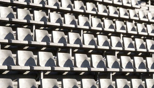 Empty stadium bleachers with light-gray bucket seats casting geometric shadows