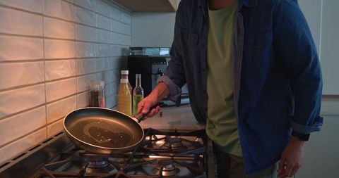 Mid-adult man tilting nonstick pan on gas stove heating oil in cozy modern kitchen