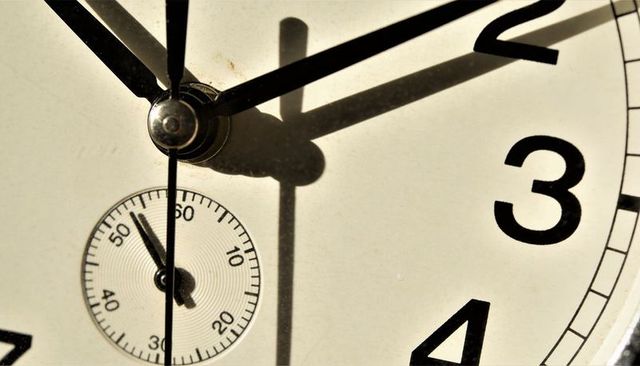 Macro vintage clock face with patina, hub and hands casting dramatic shadows, close-up