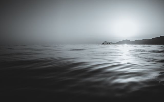 Monochrome scene captures the calmness of dawn with gentle waves on the ocean and distant hills. Ideal for use in travel-related content, relaxation themes, backgrounds for nature articles, or inspiration for tranquil living.