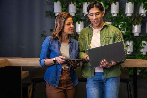 Diverse coworkers collaborating in modern office lounge using laptop and tablet