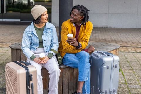 Young Travelers Sharing Coffee While Waiting with Luggage Outside