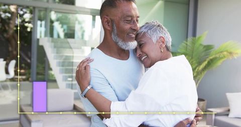 Senior couple embracing near glass doors in modern home showing warm companionship and joy