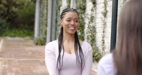 Smiling woman chatting with friend in courtyard wearing pink top and hoop earrings