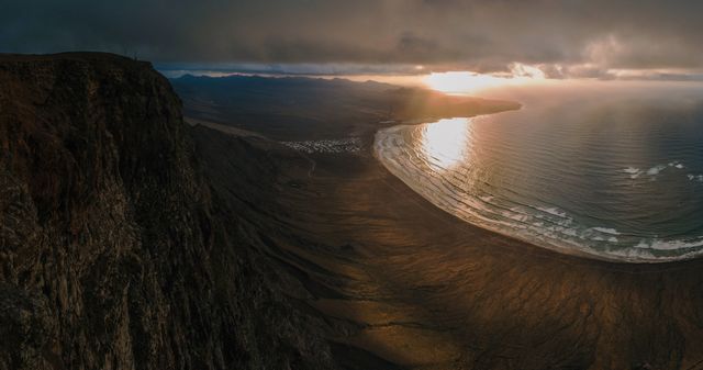 Picture shows a stunning sunset over a coastal landscape with steep rocky cliffs and the ocean below, waves gently crashing onto shore. Ideal for use in travel promotions, nature documentaries, motivational posters, and websites sharing scenic views and outdoor adventures.