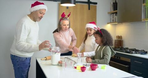 Family baking holiday cookies in kitchen wearing Santa hats and festive reindeer headbands