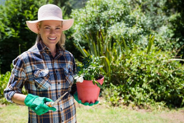 Woman enjoying gardening on a sunny day, holding a sapling and trowel. Ideal for use in articles about gardening, outdoor hobbies, and healthy lifestyles. Perfect for promoting gardening tools, outdoor activities, and nature-related content.