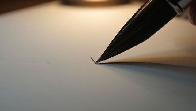 Fountain Pen Nib Touching Paper Forming Small Folded Corner Under Warm Desk Light