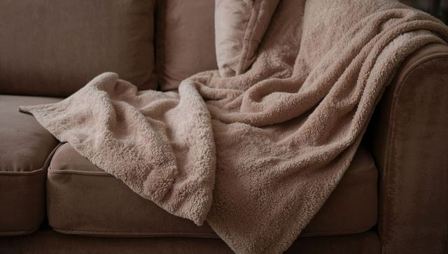 Cozy beige sherpa throw draped over taupe velvet sofa, soft plush texture and folds