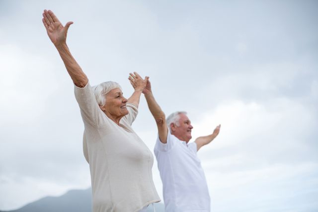 Smiling senior couple standing with arms outstretched on the beach