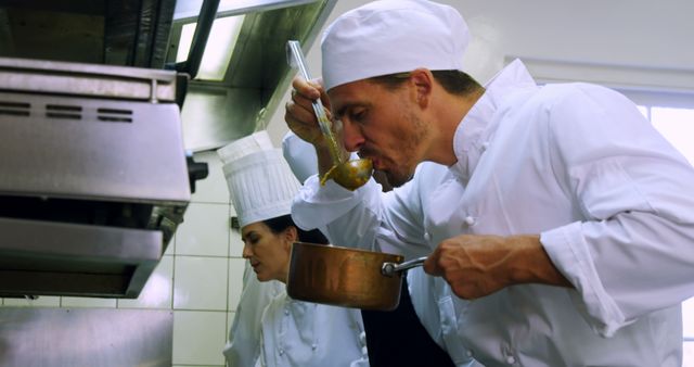 Professional chef in a commercial kitchen deeply focused on tasting food. Perfect for content relating to culinary arts, restaurant work, kitchen teamwork, and professional cooking techniques.