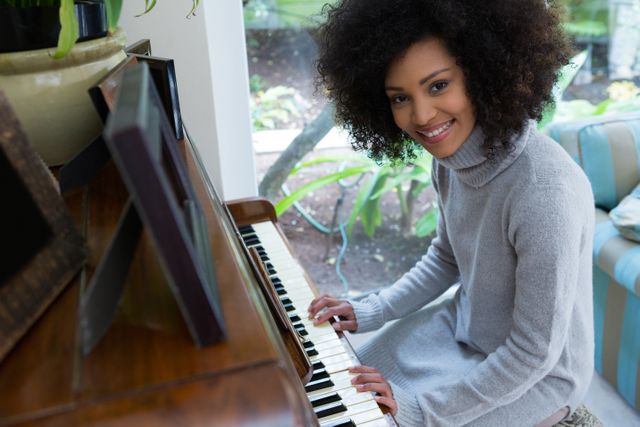 This image shows a woman with curly hair playing the piano at home. She is smiling and appears to be enjoying herself. This image can be used for articles or advertisements related to music, home activities, hobbies, relaxation, and creative pursuits.