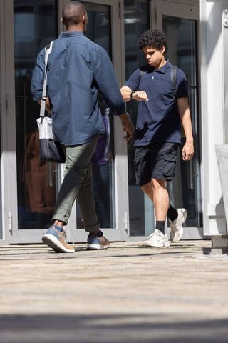 Two young men walking past glass doors checking wristwatch and carrying bags