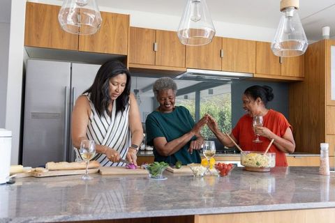 Multigenerational friends preparing meal and sharing wine at modern kitchen island