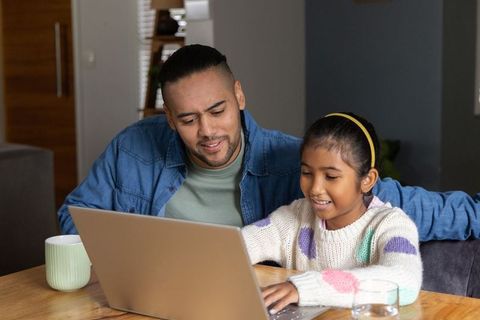 Diverse father and daughter collaborating on laptop at cozy home workspace