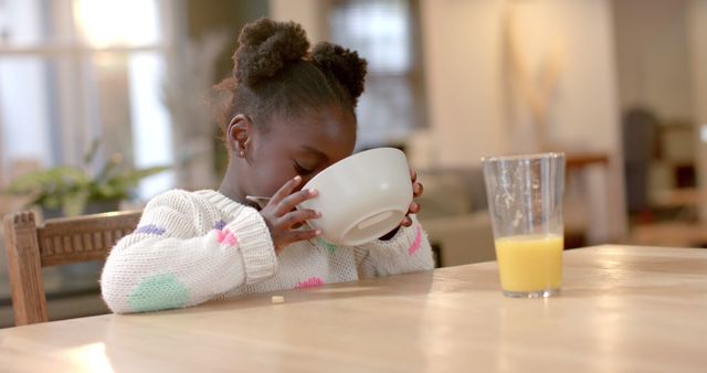 Young Girl Drinking from Bowl Sitting at Table with Glass of Orange Juice - Download Free Stock Images Pikwizard.com