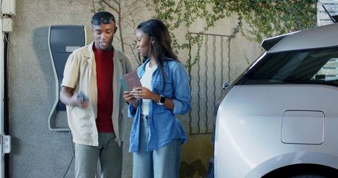 Stylish Couple Charging Electric Vehicle Before Eco-Friendly Adventure