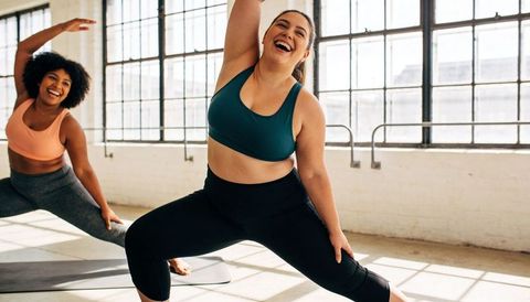 Joyful body-positive workout stretching in sunlit urban studio with mats and barre