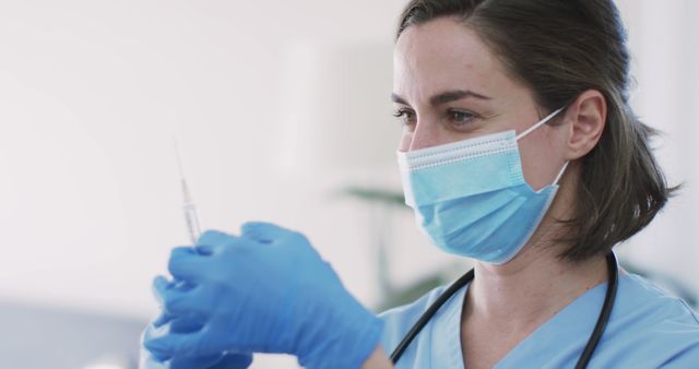 Female nurse wearing protective face mask and gloves, carefully preparing a vaccine syringe. Ideal for use in healthcare articles, vaccination campaigns, and medical training materials.