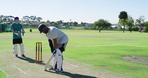 Adult batsman adjusting stance on suburban cricket pitch wearing helmet and pads