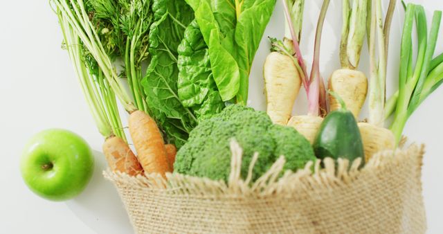 Fresh organic vegetables including carrots, broccoli, parsnips, and leafy greens along with a green apple spilling out of a burlap bag. Perfect for illustrating concepts of healthy eating, farm-to-table, vegetarian or vegan lifestyles, and cooking ingredients.