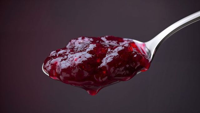 Berry jam glistening on spoon against dark backdrop