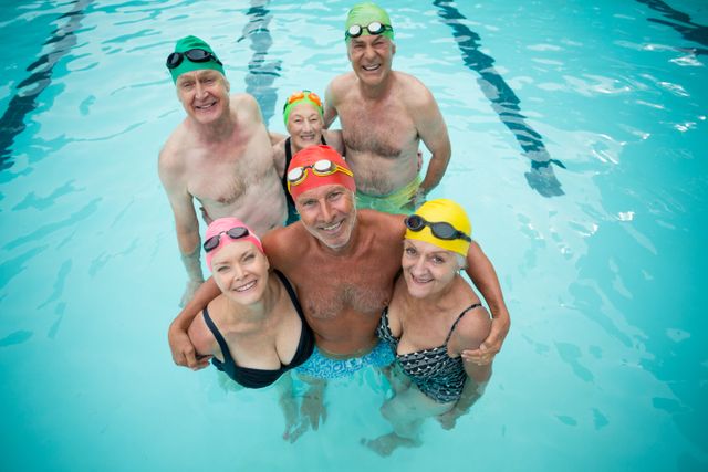 Group of senior swimmers standing in a swimming pool, smiling and wearing colorful swim caps. Ideal for promoting active senior lifestyles, fitness programs for the elderly, and aquatic exercise classes. Can be used in health and wellness campaigns, retirement community advertisements, and sports-related content.