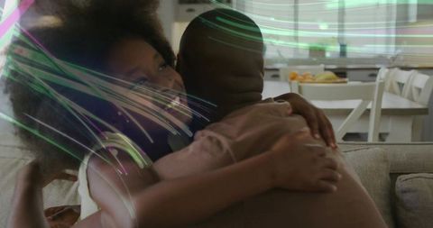 Man hugging smiling girl on sofa in sunlit living room with light streaks