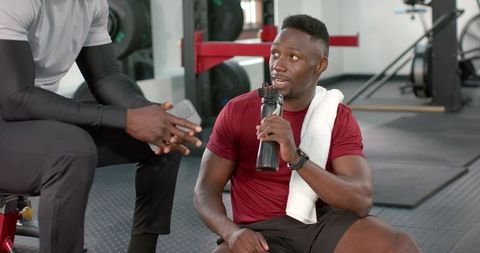 African american trainer coaching client in gym during workout holding water bottle