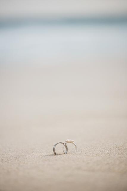 Romantic scene of two wedding rings lying on sandy beach, symbolizing love and commitment. Perfect for wedding invitations, beach wedding promotions, and romantic vacation advertisements.