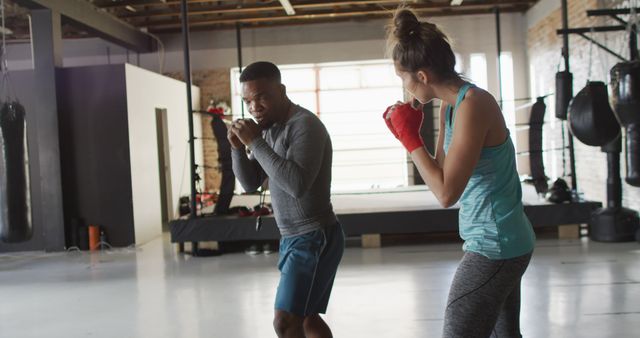 Male trainer and female trainee practicing boxing techniques in modern, well-equipped gym. Perfect for articles, promotional materials for boxing classes, fitness blogs, or personal training advertisements.