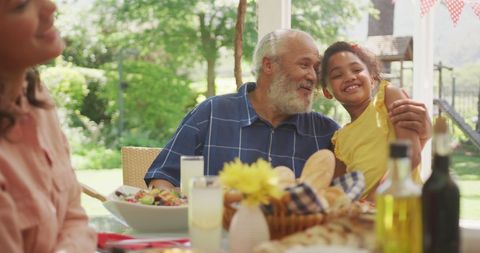 Happy diverse mother, daughter and grandfather talking at family dinner table in sunny garden - Download Free Stock Photos Pikwizard.com