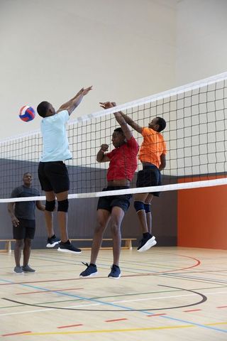 African american men jumping to block red white blue volleyball in indoor gym competition