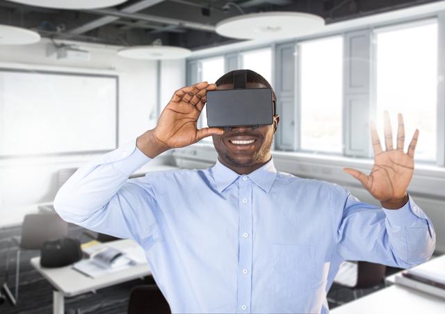 Man using virtual reality headset in a modern office, smiling and engaging with the virtual environment. Ideal for illustrating concepts of technology in the workplace, innovation, digital transformation, and immersive experiences in business settings. Suitable for articles, presentations, and marketing materials related to VR technology and its applications in professional environments.