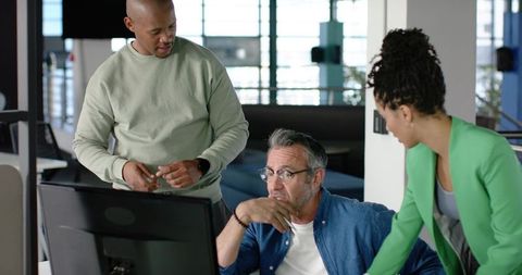 Diverse team collaborating around monitor in modern open-plan office, brainstorming ideas