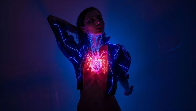Woman wearing cropped jacket emitting neon heart projection and glowing blue veins