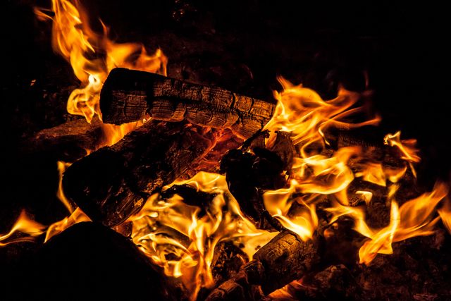 Close-up view of glowing campfire flames at night. Depicts warmth and rustic outdoor experience. Ideal for use in articles or media related to camping, outdoor adventures, survival skills, or fire safety tutorials.