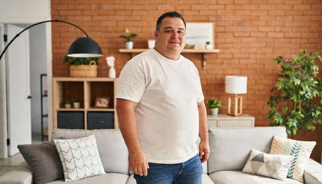 Confident man standing in cozy brick living room wearing white t-shirt and jeans