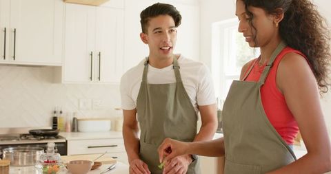 Young Couple Preparing Meal Together in Modern Bright Kitchen Wearing Matching Aprons