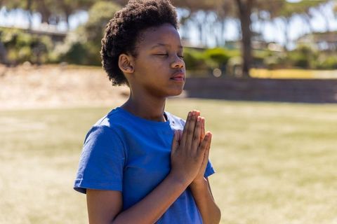 African american child practicing mindful prayer and meditation on sunlit park field