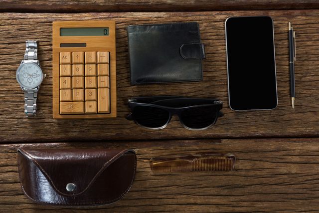 Various men's accessories including a watch, wooden calculator, black wallet, smartphone, sunglasses, pen, comb, and leather case arranged neatly on a rustic wooden surface. Ideal for use in lifestyle blogs, fashion articles, organizational tips, or product advertisements.
